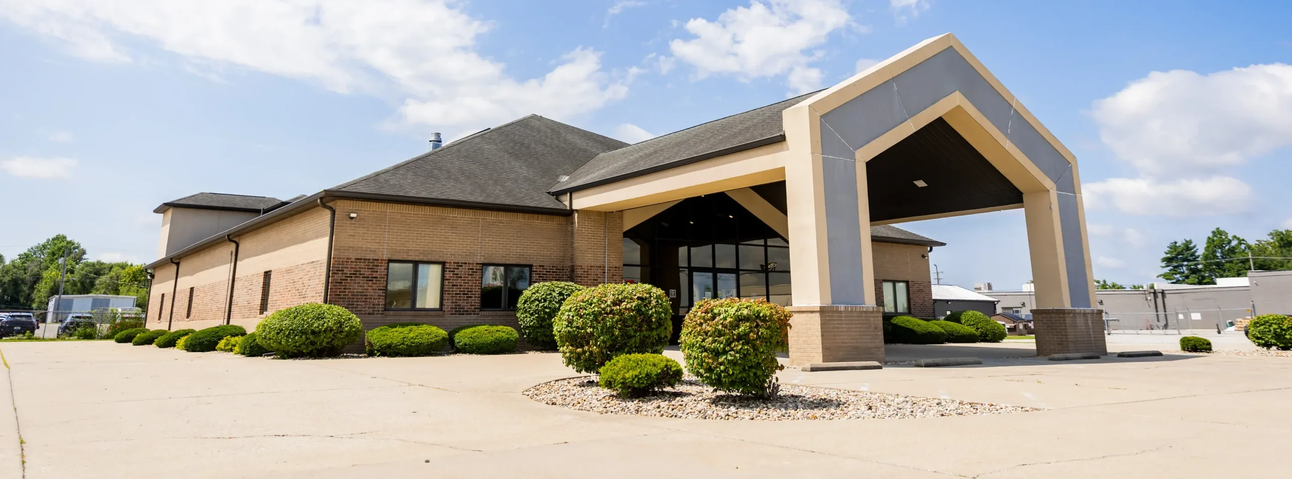 Indiana Center for Recovery Terre Haute facility exterior featuring a modern brick building with a covered entrance, landscaping, and bright blue sky.