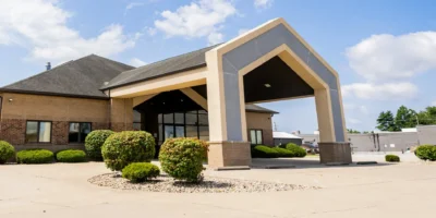Indiana Center for Recovery Terre Haute facility exterior featuring a modern brick building with a covered entrance, landscaping, and bright blue sky.