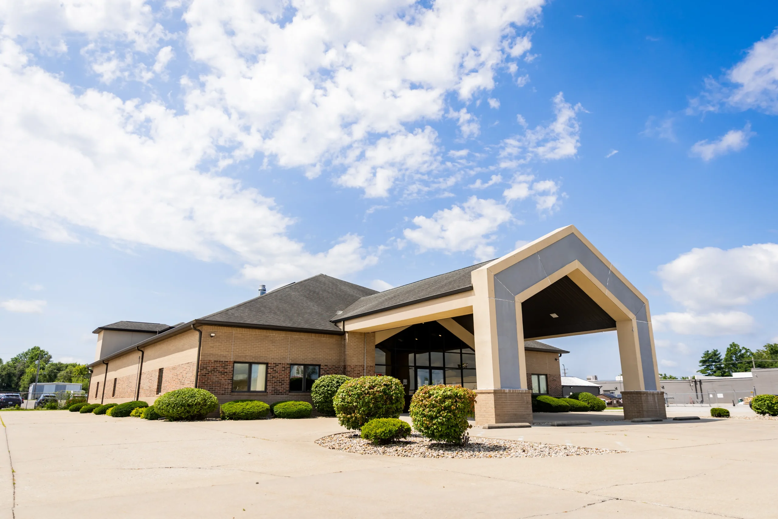 Indiana Center for Recovery Terre Haute facility exterior featuring a modern brick building with a covered entrance, landscaping, and bright blue sky.