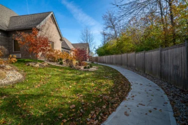 Curved walking path behind the Indiana Center for Recovery building, bordered by fall landscaping and a tall wooden privacy fence.