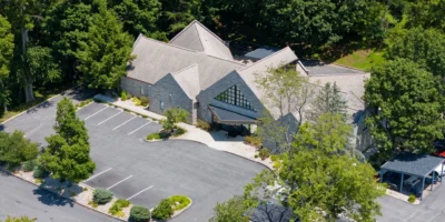 Aerial drone view of Indiana Center for Recovery Bloomington showing the stone building surrounded by trees, with a curved driveway and mostly empty parking lot.