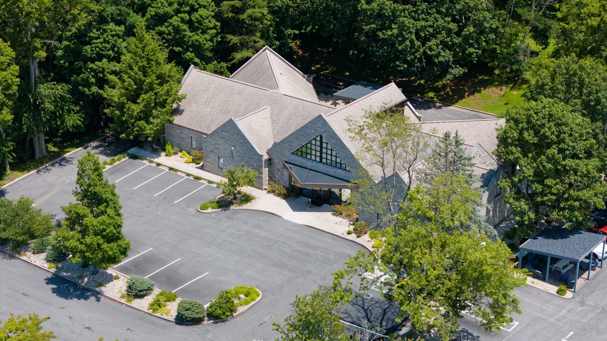 Aerial drone view of Indiana Center for Recovery Bloomington showing the stone building surrounded by trees, with a curved driveway and mostly empty parking lot.