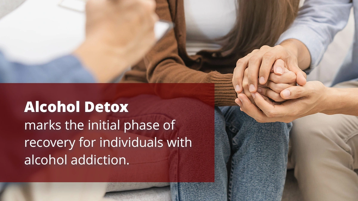 
A text box on the left reads, "Alcohol Detox marks the initial phase of recovery for individuals with alcohol addiction." On the right, the image shows a close-up of two people holding hands, offering support and comfort. The setting suggests a therapy or counseling session, with the focus on the compassionate and supportive interaction between the individuals.