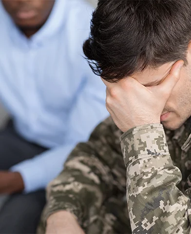 A soldier in uniform sits alone in a dimly lit room, looking distressed and absorbed, highlighting the emotional struggles.