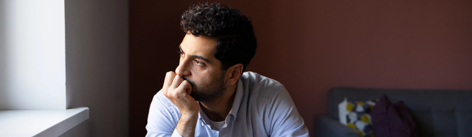 Sad man looking at of a window while he rests his chin on his palm