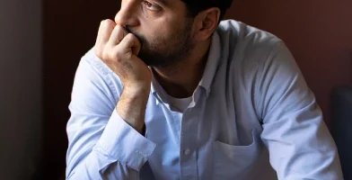 Sad man looking at of a window while he rests his chin on his palm