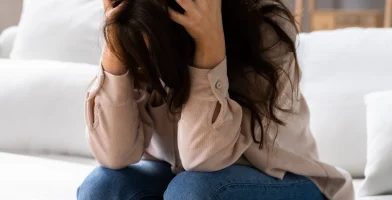 distressed woman with her hands pressed on her head as she looks down