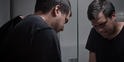 Man with great despair looking down in front of a mirror
