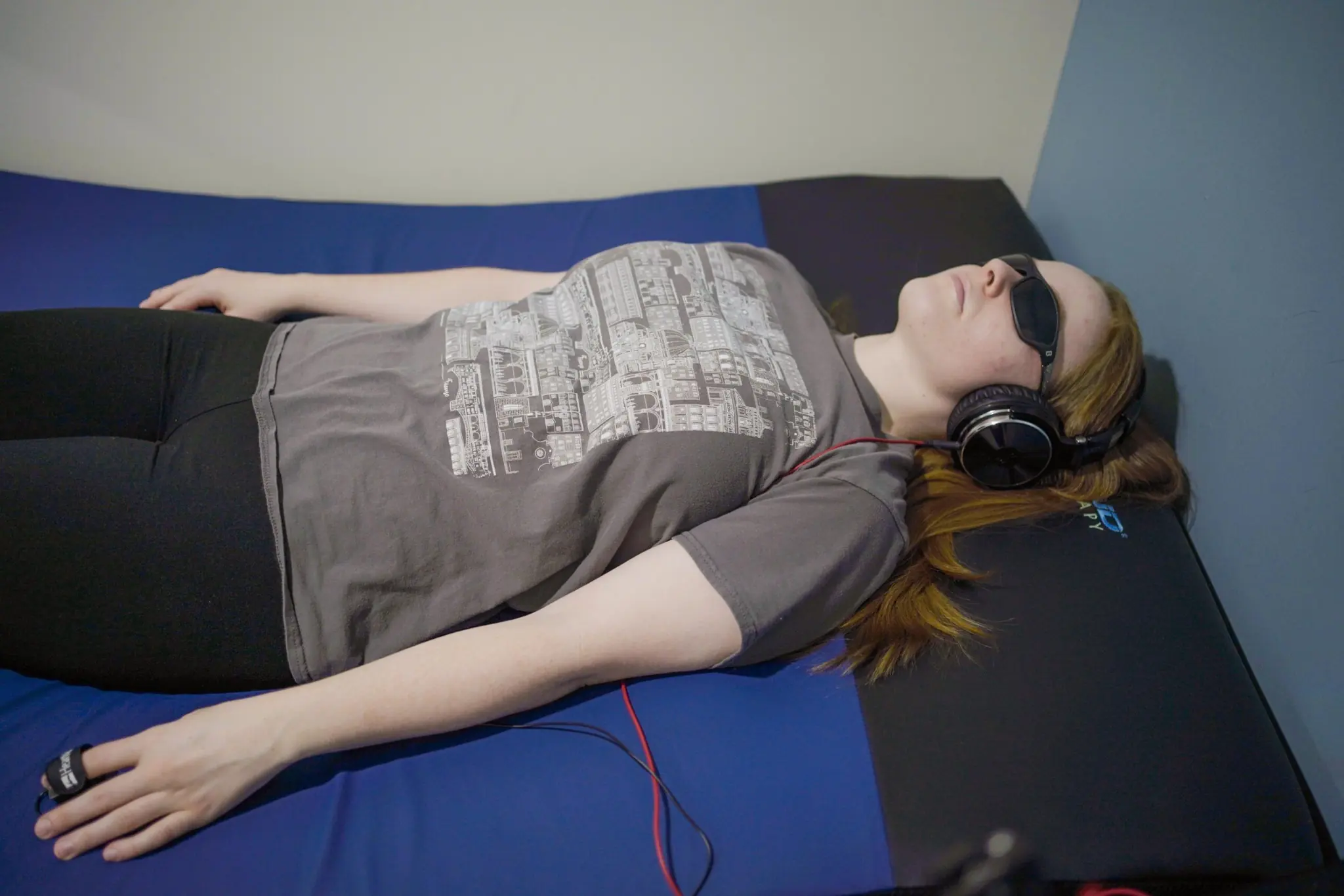 Patient lying comfortably during a biofeedback therapy session while wearing headphones and relaxation equipment in a clinical treatment room.