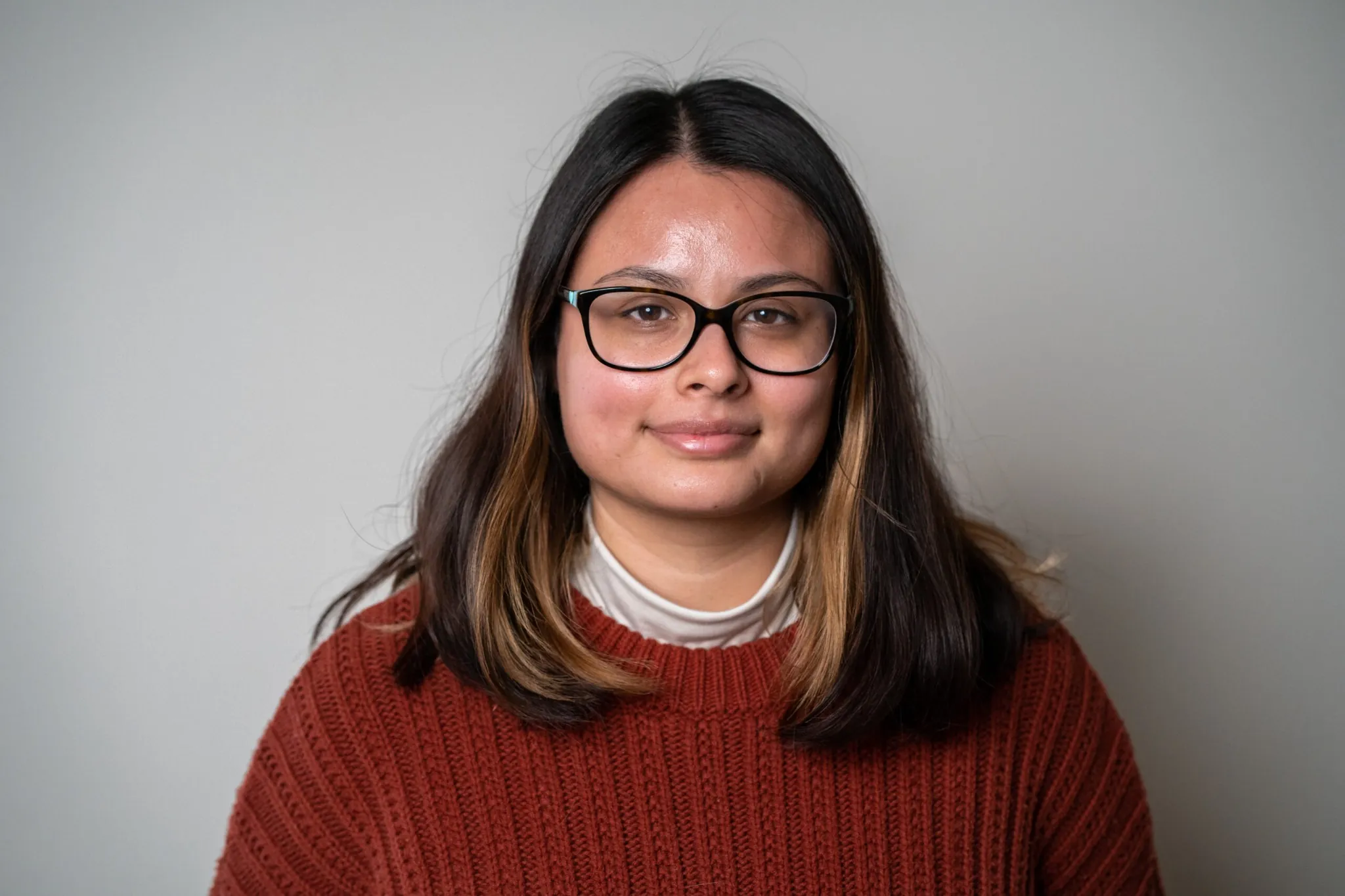Portrait of Brianny, an ICFR staff member, wearing glasses and a rust-colored sweater against a neutral background