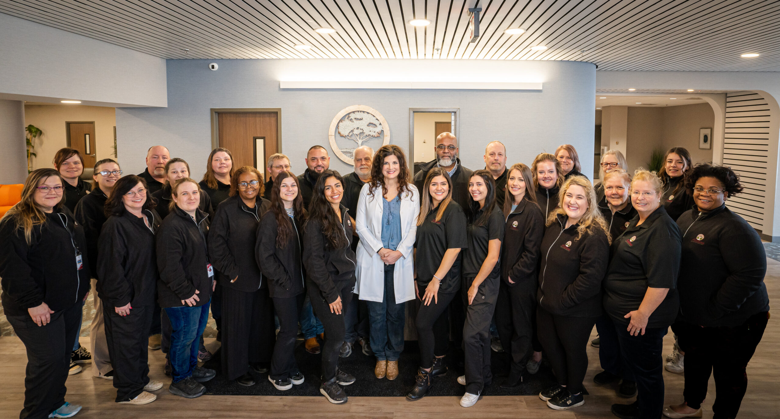 Group photo of Indiana Center for Recovery South Bend staff standing in a clinic lobby, smiling at the camera with a doctor in a white coat centered among team members in black uniforms.